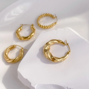 Detail of four golden twisted metal hoop earrings on minimalist white stone display