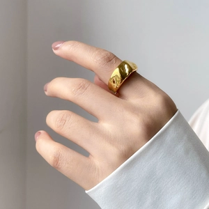 Detailed close-up of chunky gold ring with irregular lava texture on model finger