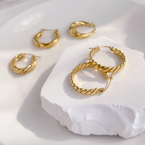 Detailed view of assorted twisted rope hoop earrings in gold finish on white marble