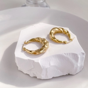 Close-up of chunky gold twisted hoop earrings on white stone background, polished finish