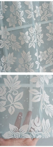 Detailed view of light blue lace curtain fabric with white floral patterns and mesh texture