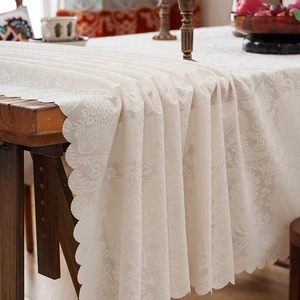 Elegant beige floral lace tablecloth with scalloped edges on a wooden table