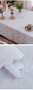 Detail of white damascus jacquard tablecloth with floral patterns and scalloped edges