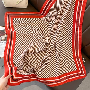 Close-up of square silk scarf with red border and geometric pattern on leather