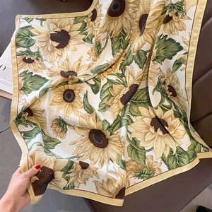 Detailed view of the sunflower print on a cream satin scarf draped over leather
