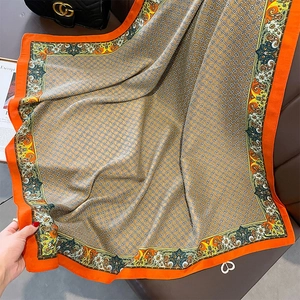 Detail view of vintage orange silk scarf with gold chain print draped on leather chair