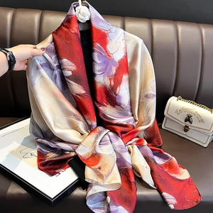 Elegant floral silk scarf with vibrant red and purple abstract patterns on leather sofa
