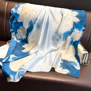Elegant satin floral scarf in sky blue and white draped over a luxury leather sofa