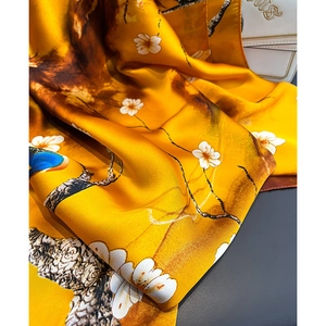 Vista macro di una sciarpa in seta gialla con fiori di prugno e motivi a pavone