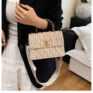Detail of bamboo handle and gold twist lock on cream quilted pleated crossbody bag