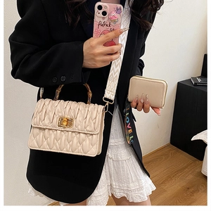 Chic quilted beige handbag with bamboo handle and wide patterned strap shown on a model