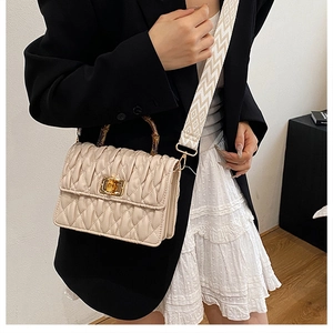 Detail of off-white quilted crossbody bag with bamboo handle and woven shoulder strap