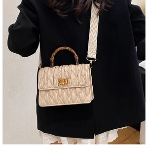 Detail of beige quilted bag with brown bamboo handle and woven wide shoulder strap