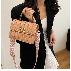 Detail of beige quilted bag with bamboo handle and wavy patterned fabric shoulder strap