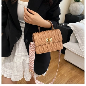 Detailed shot of khaki pleated bag featuring bamboo handle and geometric webbing strap