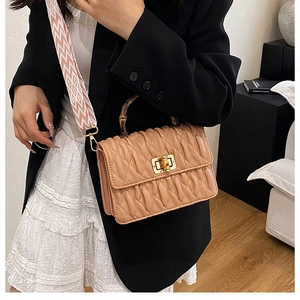 Close-up of quilted beige handbag with bamboo handle and patterned strap on a model