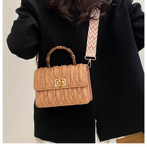 Detail of quilted crossbody bag with bamboo handle and patterned woven strap on model