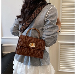 Detail of a brown pleated handbag featuring a bamboo handle and geometric patterned strap