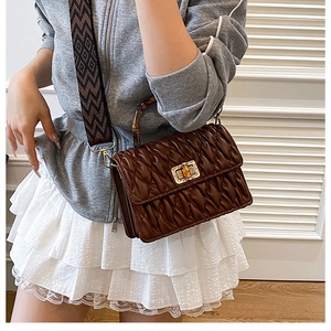 Detail of bamboo handle and pleated brown leather bag with geometric woven strap