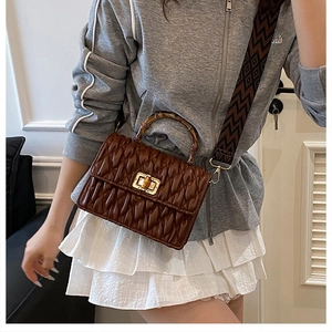 Detail of brown pleated handbag with bamboo handle and patterned wide strap on a model