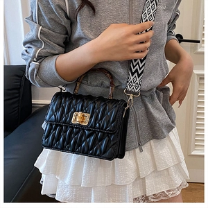 Detail of quilted black leather bag with bamboo handle and golden twist-lock closure