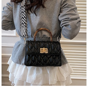 Detail of bamboo handle and gold turn-lock closure on black ruched crossbody bag
