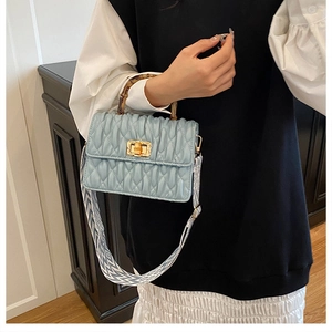Detail of light blue quilted bag featuring natural bamboo handle and gold twist lock clasp