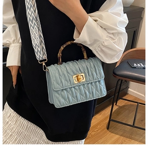 Detail of light blue crossbody bag with bamboo handle and patterned wide strap