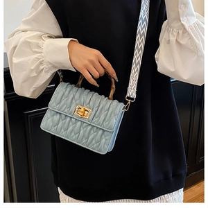 Detail of light blue quilted handbag featuring bamboo handle and golden twist-lock closure
