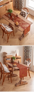 Detail of burnt orange table runner with gold feather prints and wavy edges on a wooden table