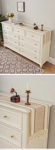 Detail of woven table runner with natural stripes and handmade tassels on white cabinet