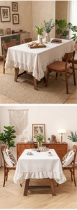 Detail of beige linen tablecloth with ruffled edges on a rectangular wooden table