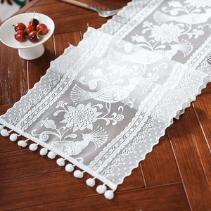 Detailopname van witte kanten tafelloper met bloemmotieven en decoratieve pomponfranjes