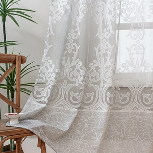Light gray damask lace curtain with leaf patterns in a cozy, sunlit living room