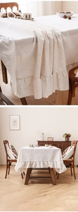 Dettaglio del bordo a balze su tovaglia in lino beige con esposizione in sala