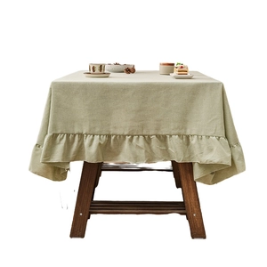 Minimalist sage green linen tablecloth with ruffled edges on a vintage wooden table