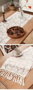 Detail of white crochet floral lace table runner with elegant tassels on wood