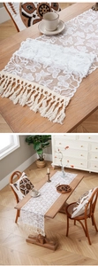 Close-up of white lace table runner with butterfly patterns and long fringe tassels