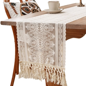 Elegant white lace table runner with fringe tassels on a rustic dark wood dining table