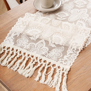 Elegant cream lace table runner with floral hollow patterns and tassels on a wooden table