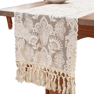 Elegant cream lace table runner with tassels draped over a vintage wooden dining table