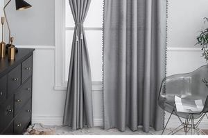 Detail of grey blackout curtains featuring decorative pom-pom trim and tassel tiebacks