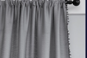Close-up of grey textured curtain with decorative pom-pom fringe edges on a black rod