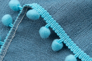 Detailed macro view of lake blue faux linen curtain fabric with matching pom-pom trim edge