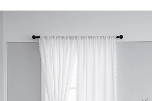 Detail of white semi-sheer kitchen curtain featuring decorative pom-pom fringe trim