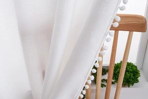 Close-up of white semi-sheer cotton linen curtain with decorative pompom fringe trim