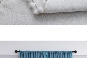Detail of fabric curtains with pom-pom trim showing textured gray and blue material