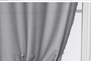 Detail of grey curtain featuring brushed texture fabric and decorative pom-pom trim edge