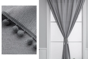 Detail of grey linen textured curtain featuring decorative pom-pom fringe and matching tieback
