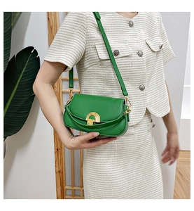 Détail du sac de selle vert en cuir avec fermoir doré sur une tenue en tweed